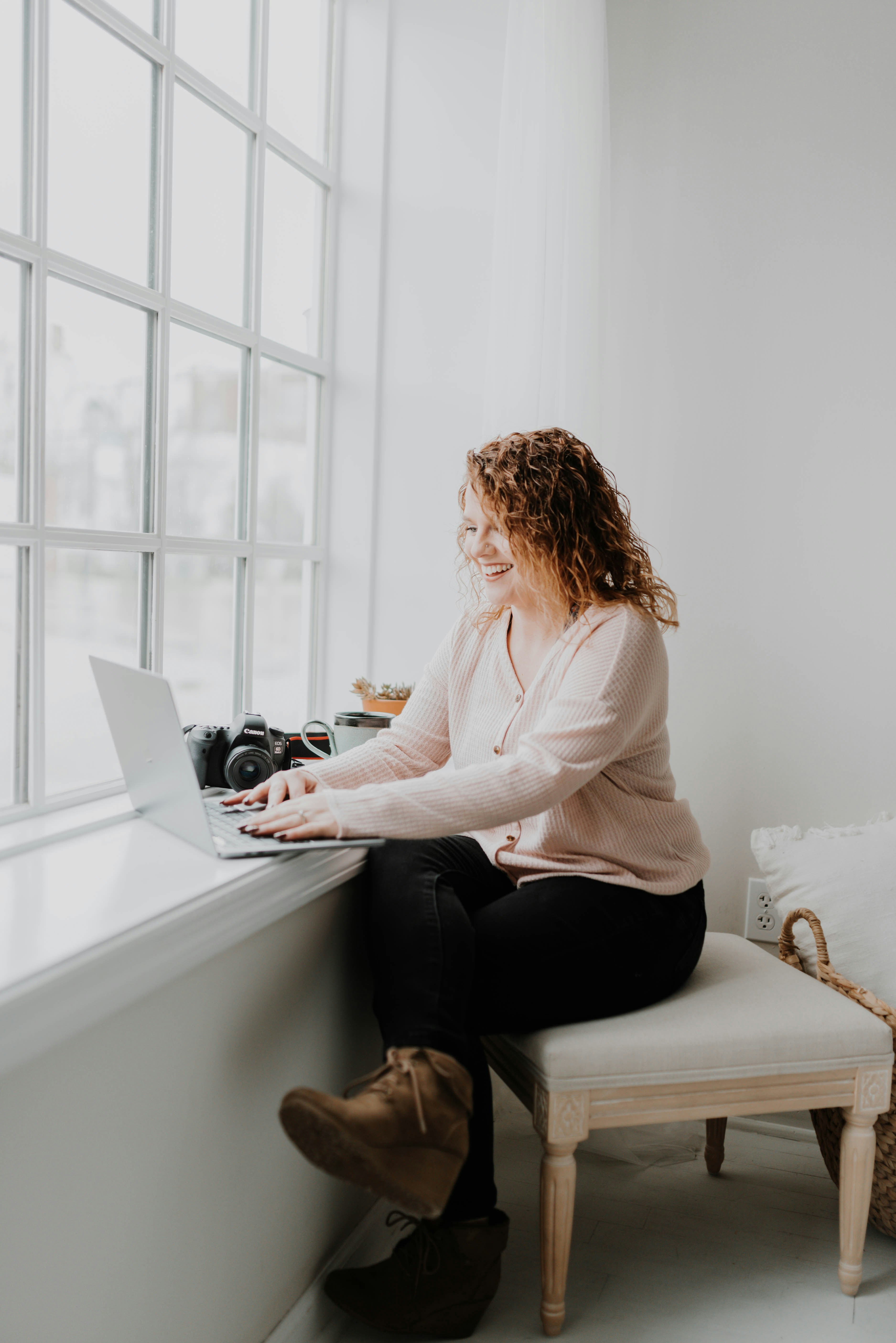 A woman in a cream cardigan working on a laptop by a sunlit window